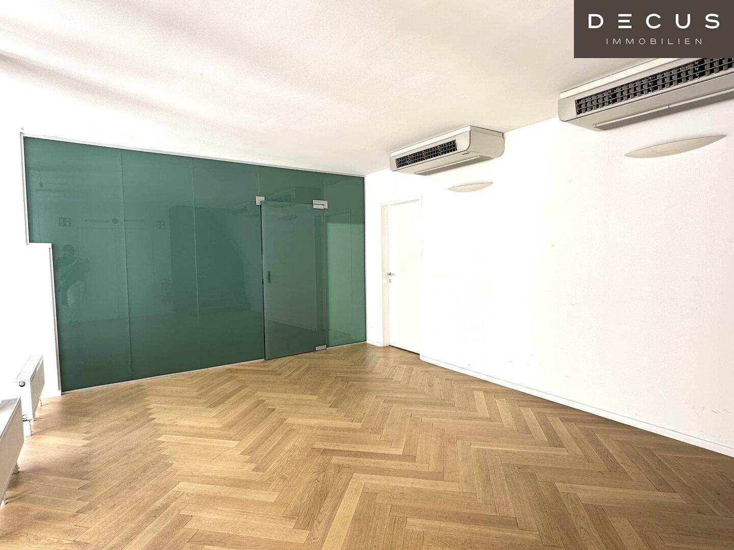 Geräumiger Büroraum mit Fischgrätparkett, Glaswänden und Klimaanlage an der Decke, angenehmes Raumklima.