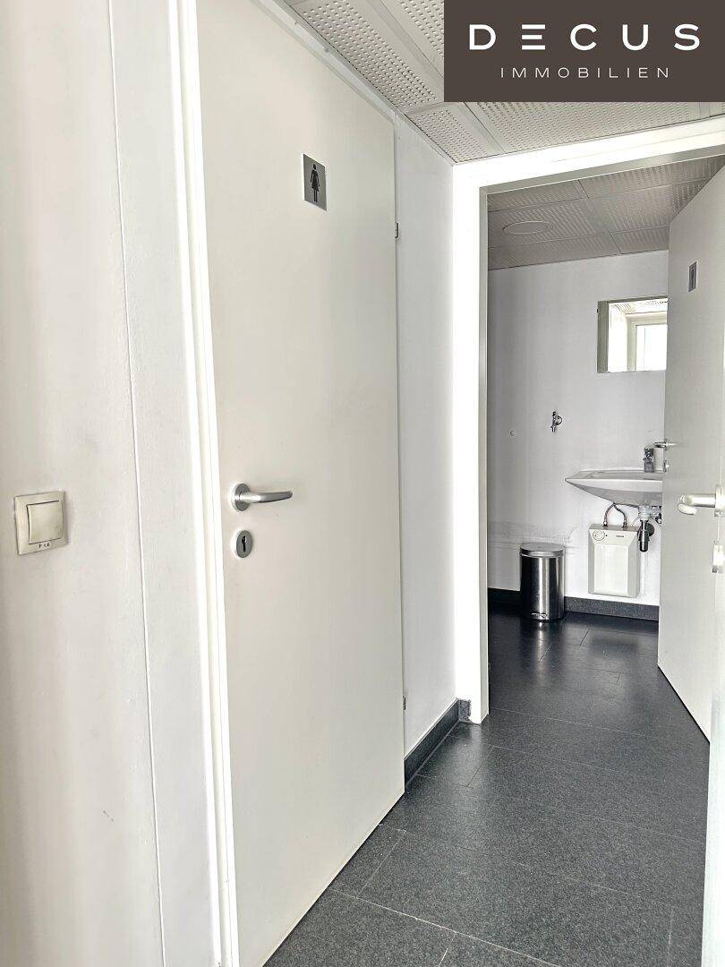 Schlichter Toilettenraum mit dunklen Fliesen, Waschbecken und einem kleinen Spiegel, funktional und sauber.