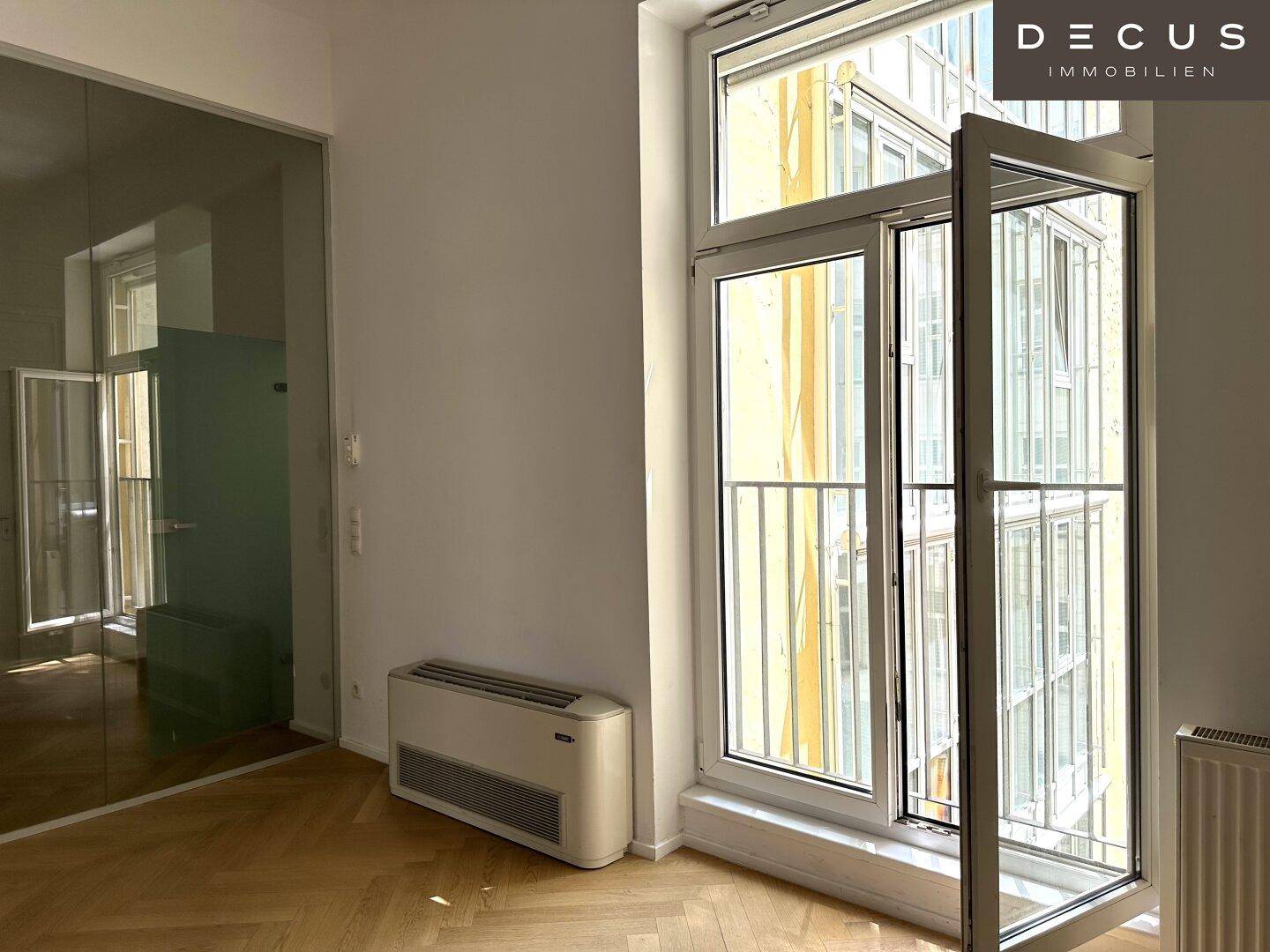 Heller Büroraum mit Fischgrätparkett, großen Fenstern und einem geöffneten Fenster, sorgt für frische Luft.