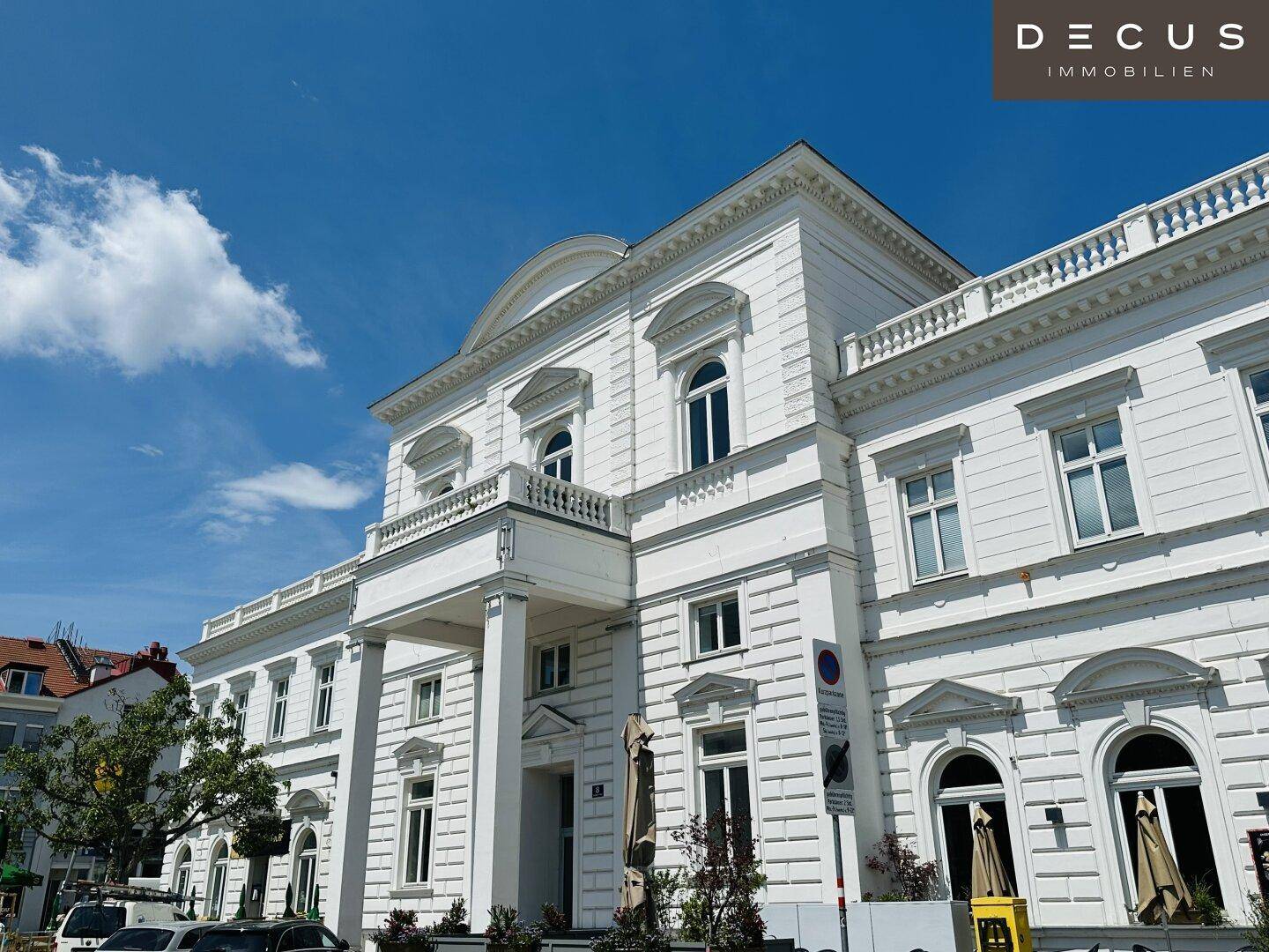 Eindrucksvolle weiße Fassade eines klassischen Gebäudes mit eleganten Verzierungen und Balkonen unter blauem Himmel.