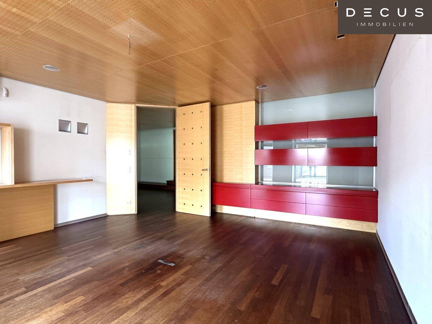 Großer offener Raum mit Holzboden, Holzlamellendecke und einer auffälligen roten Wandeinheit.
