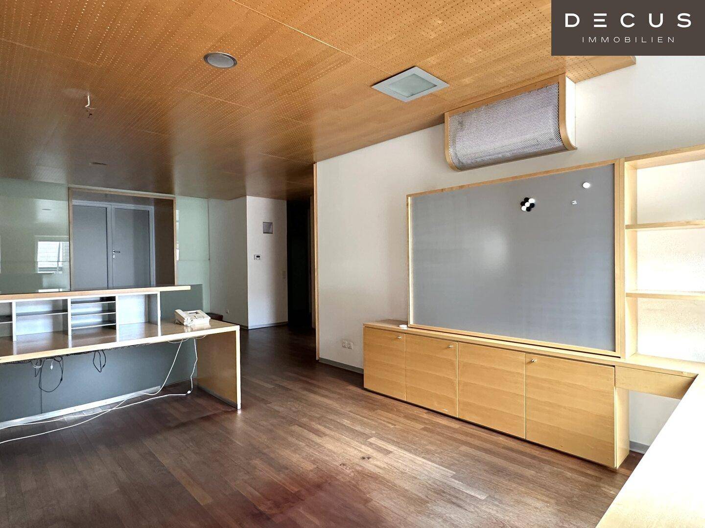 Geräumiges Büro mit Holzboden, Holzlamellendecke und einem großen, integrierten Schreibtischbereich.