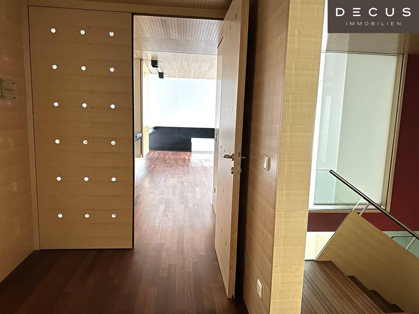 Flur mit Holzboden und Holzvertäfelung, eine offene Tür gibt den Blick in einen weiteren Raum frei.