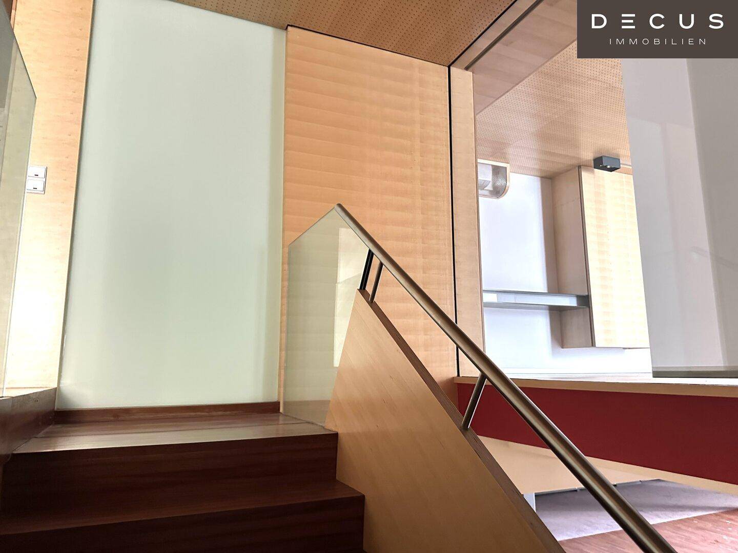 Moderne Treppe mit Glasgeländer und Holzstufen, die zu einem oberen Bereich führt.