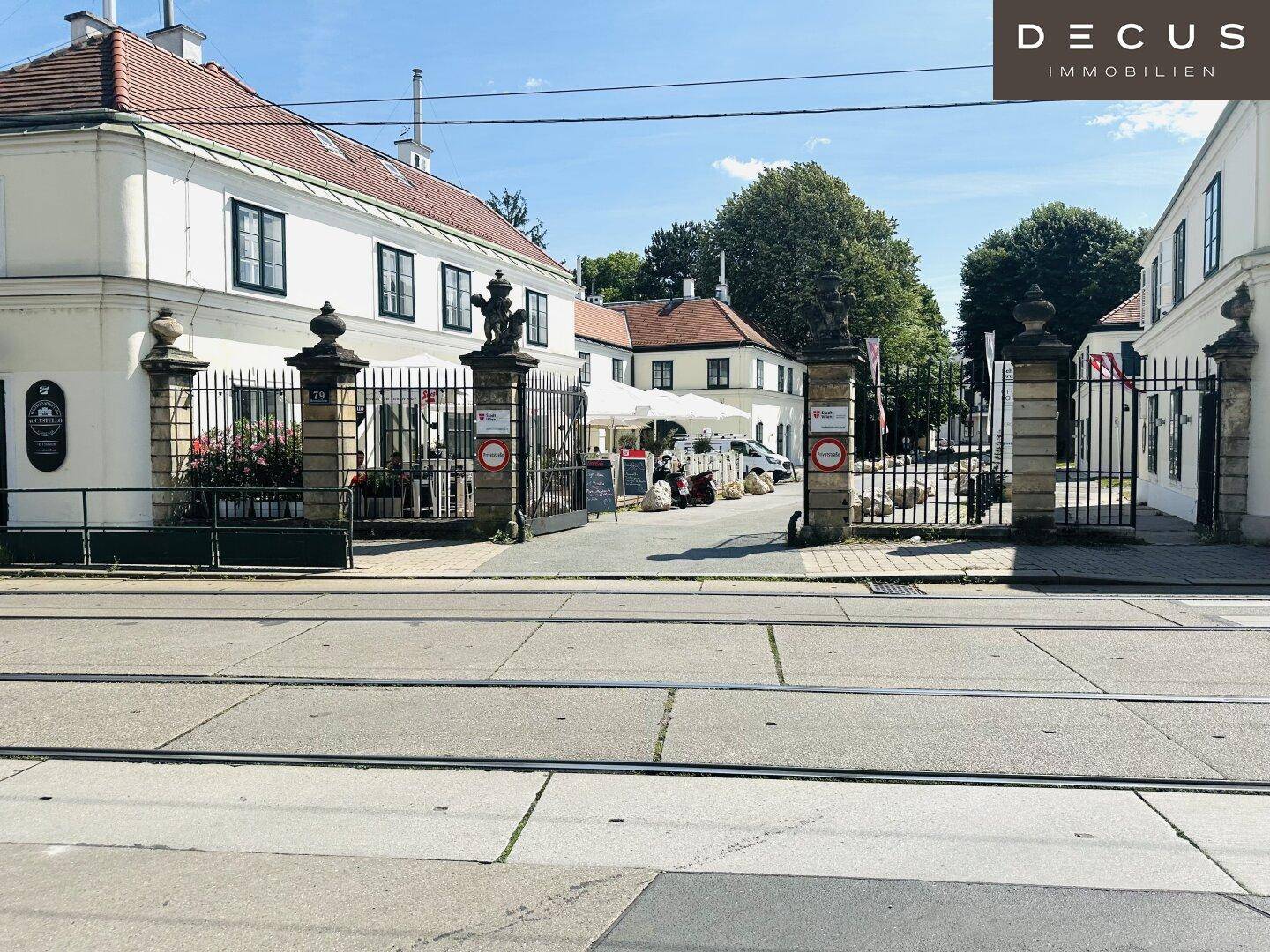 Historisches Gebäudeensemble mit Außengastronomie, umgeben von einer Straße mit Tramschienen.