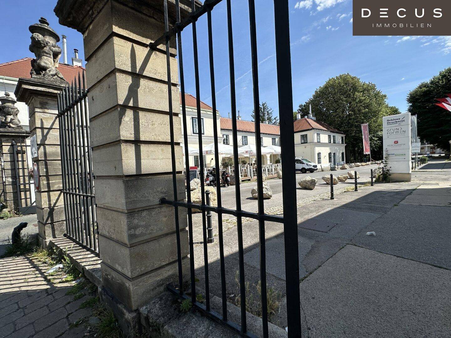 Blick durch ein schmiedeeisernes Tor auf historische Gebäude und eine belebte Straße.