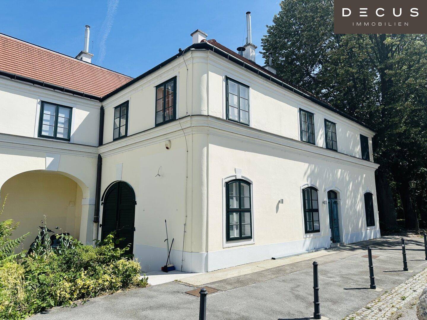 Historisches Gebäude mit weißer Fassade und grünen Fensterrahmen unter blauem Himmel.