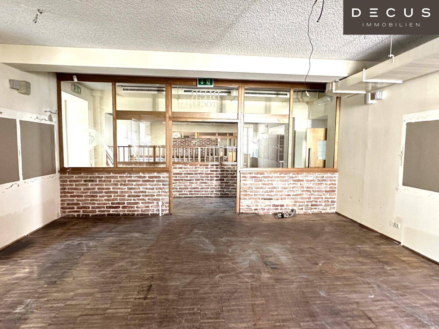 Großer Raum mit freigelegten Ziegelwänden und Holzparkett, bereit für Umbauarbeiten.