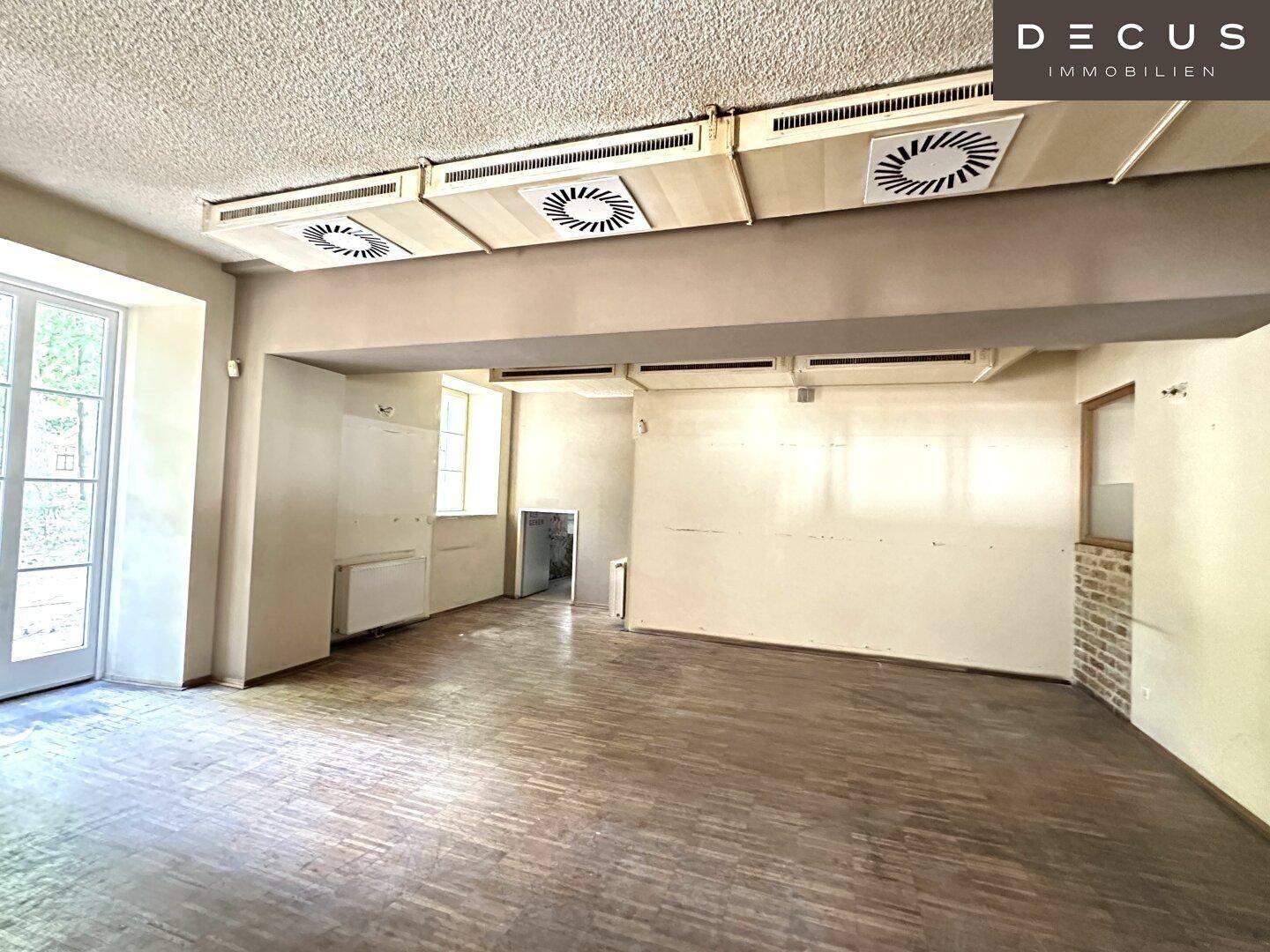 Großer, heller Raum mit Parkettboden und sichtbaren Lüftungsschächten, ideal für gewerbliche Nutzung.