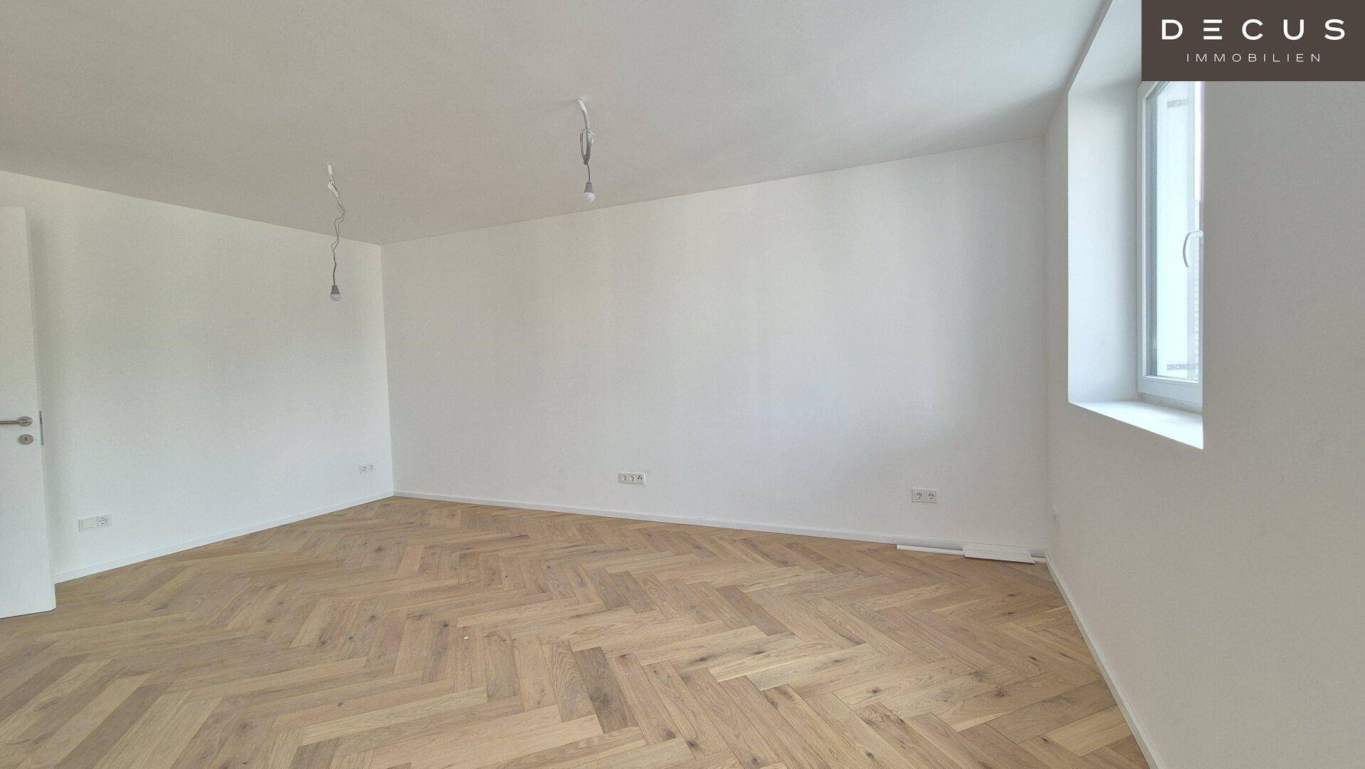 Geräumiger, heller Wohnbereich mit Fischgrätparkett und weiß gestrichenen Wänden.