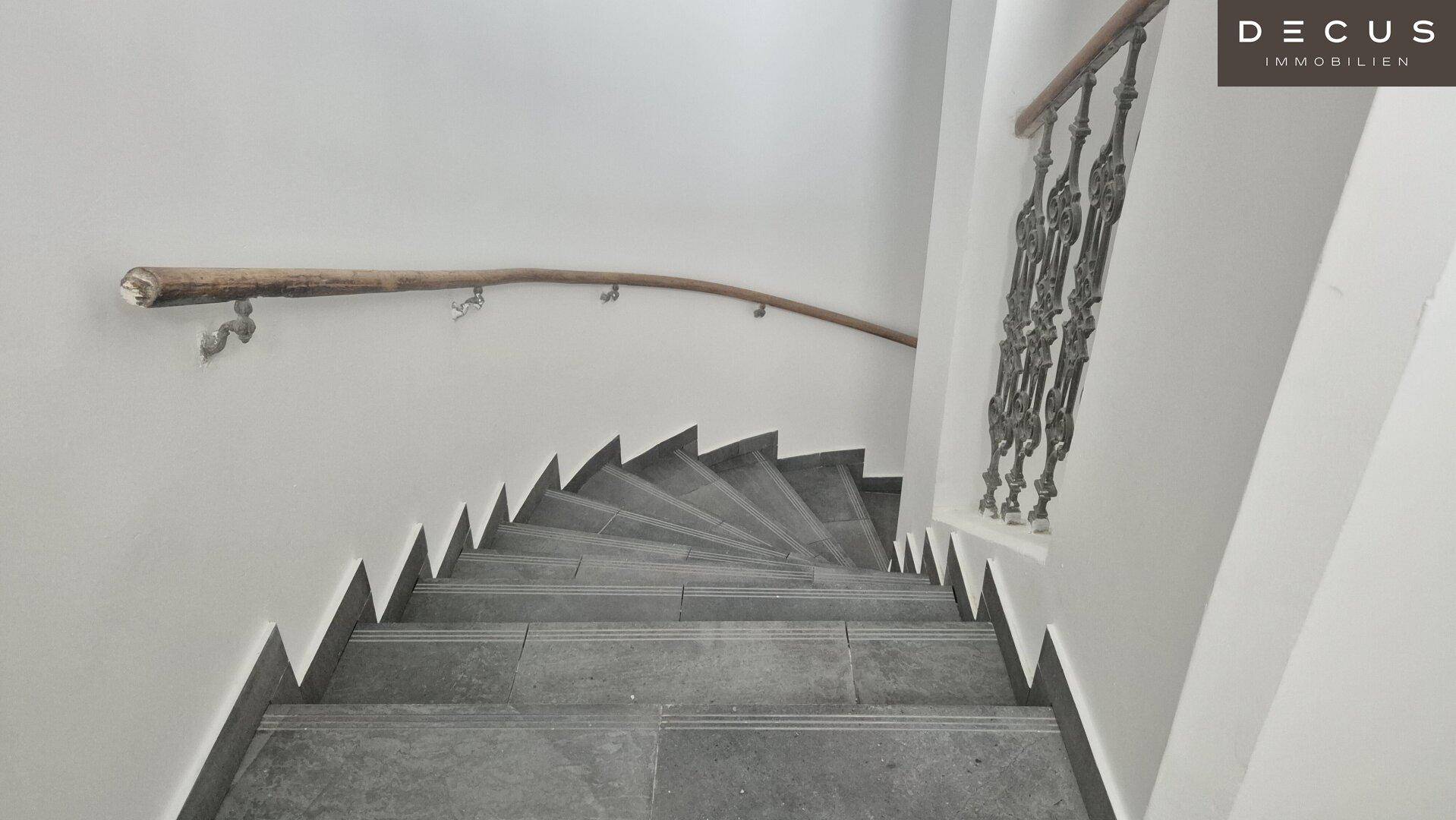 Historisches Treppenhaus mit gefliesten Stufen, schmiedeeisernem Geländer und Holzhandlauf.