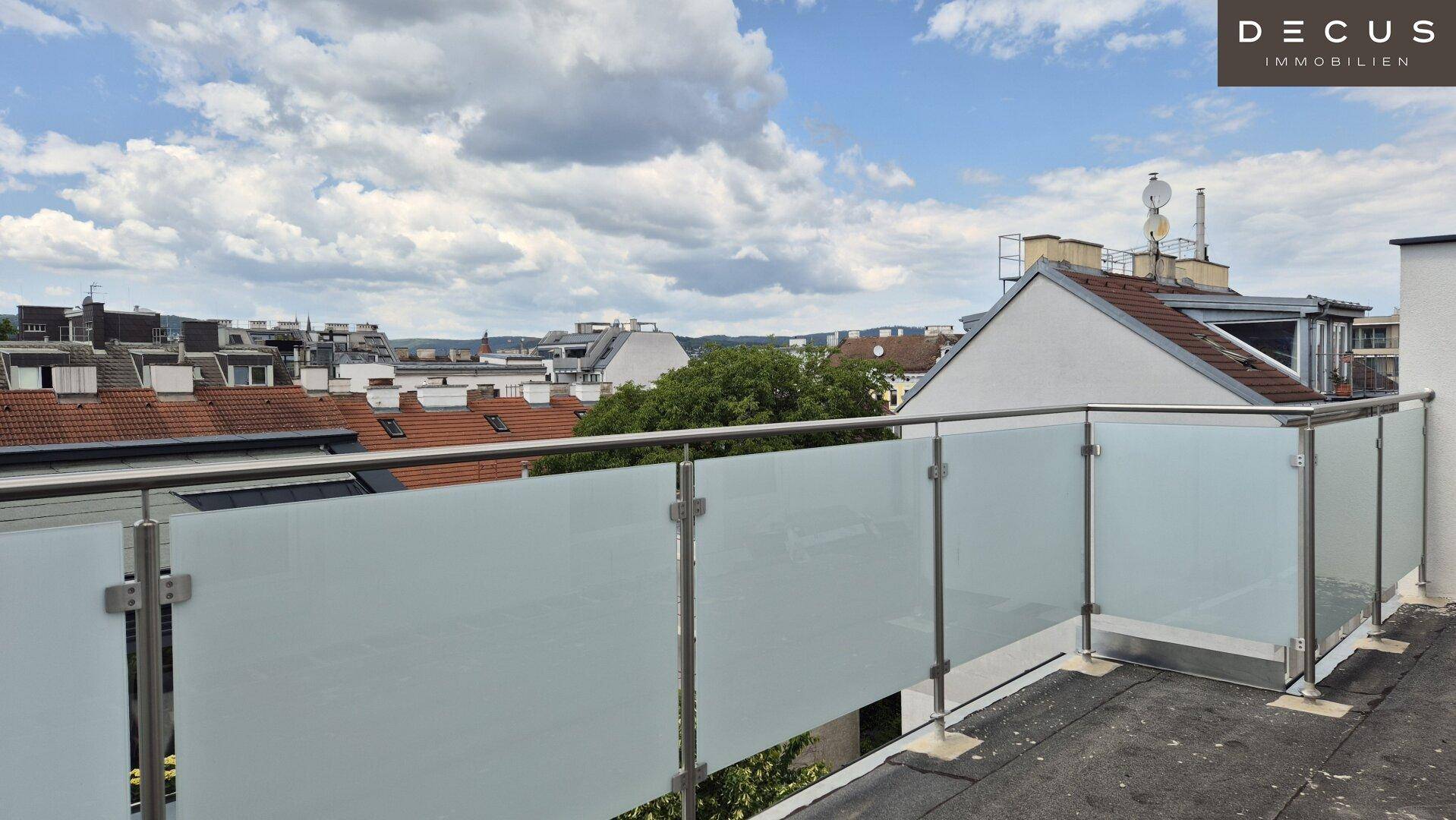 Dachterrasse mit moderner Glasbrüstung und weitem Blick über die Stadt unter bewölktem Himmel.