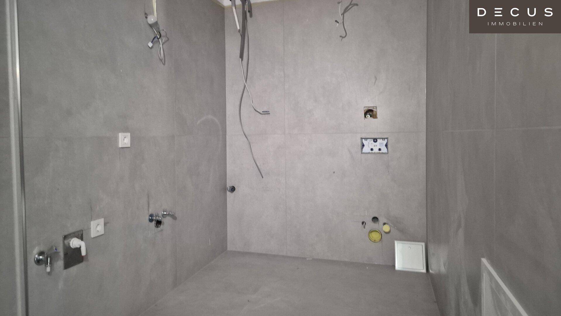 Unfertiges Badezimmer mit grauen Wand- und Bodenfliesen, bereit für den weiteren Ausbau.
