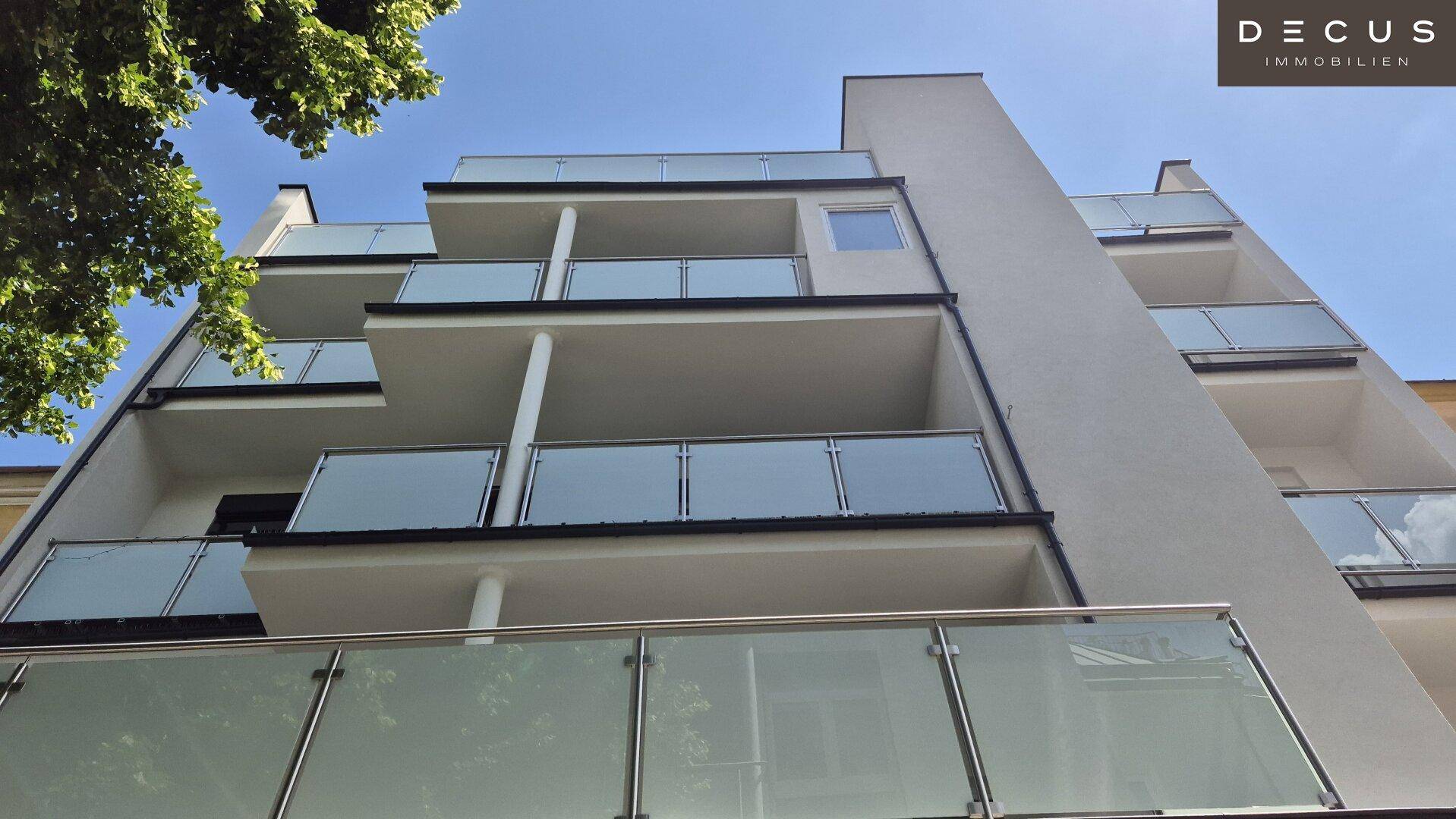 Ansicht der modernen Gebäudefassade von unten mit mehreren Balkonen und Glasgeländern unter blauem Himmel.