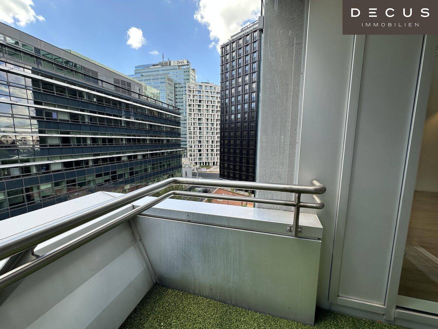 Balkon mit Kunstrasen und Panoramablick auf die umliegenden modernen Gebäude der Stadt.