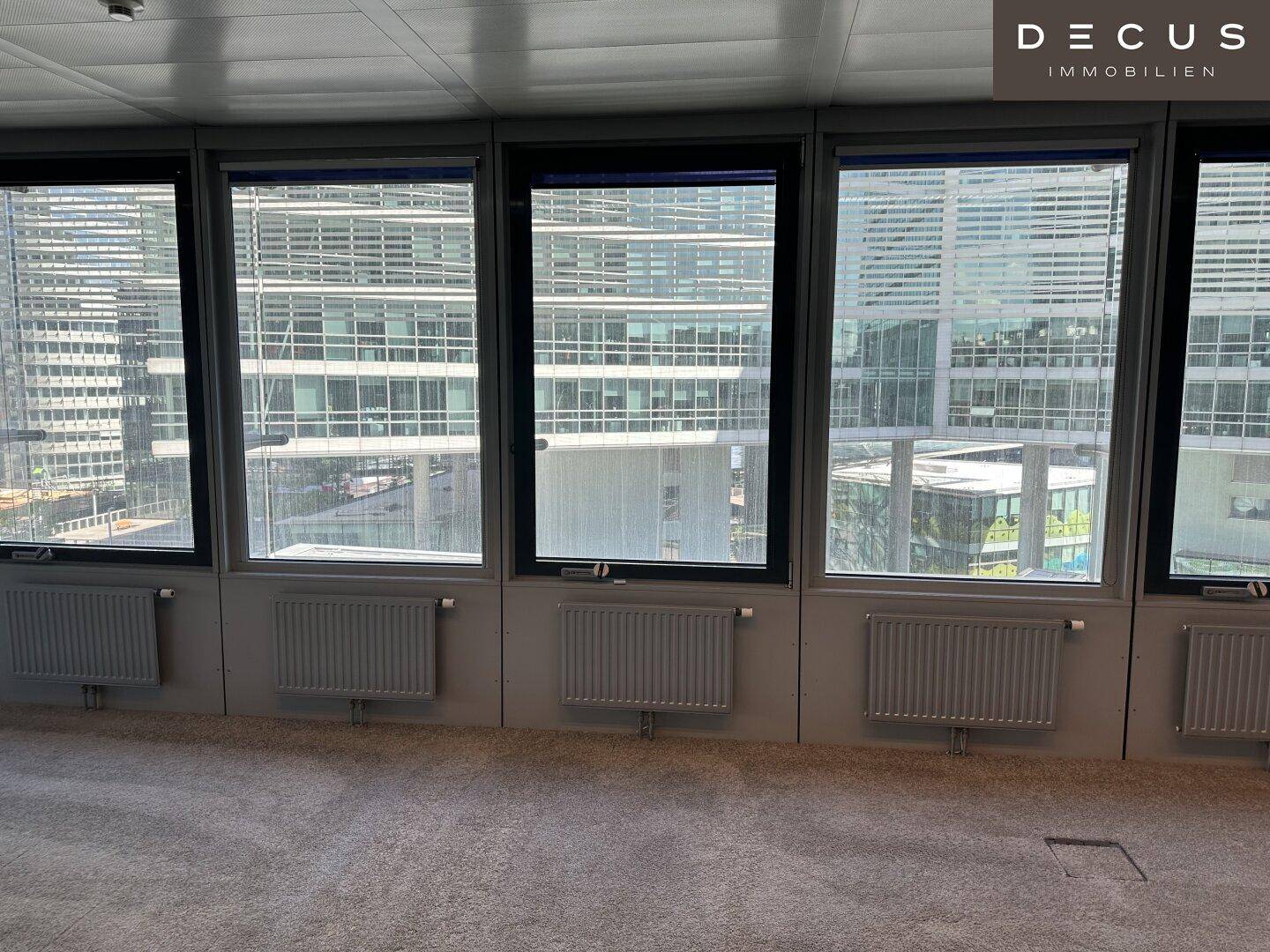 Fensterfront eines Büros mit Heizkörpern und Blick auf umliegende moderne Gebäude.
