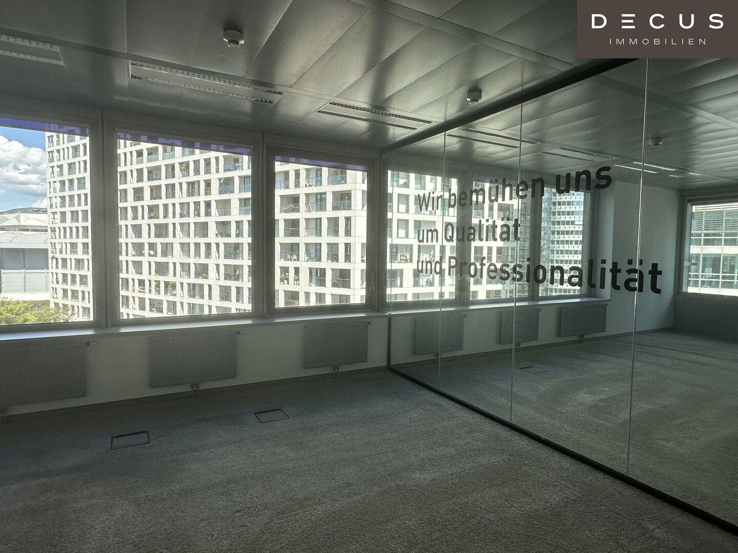 Heller Büroraum mit großen Fenstern und Teppichboden, bietet viel Tageslicht und Stadtblick.