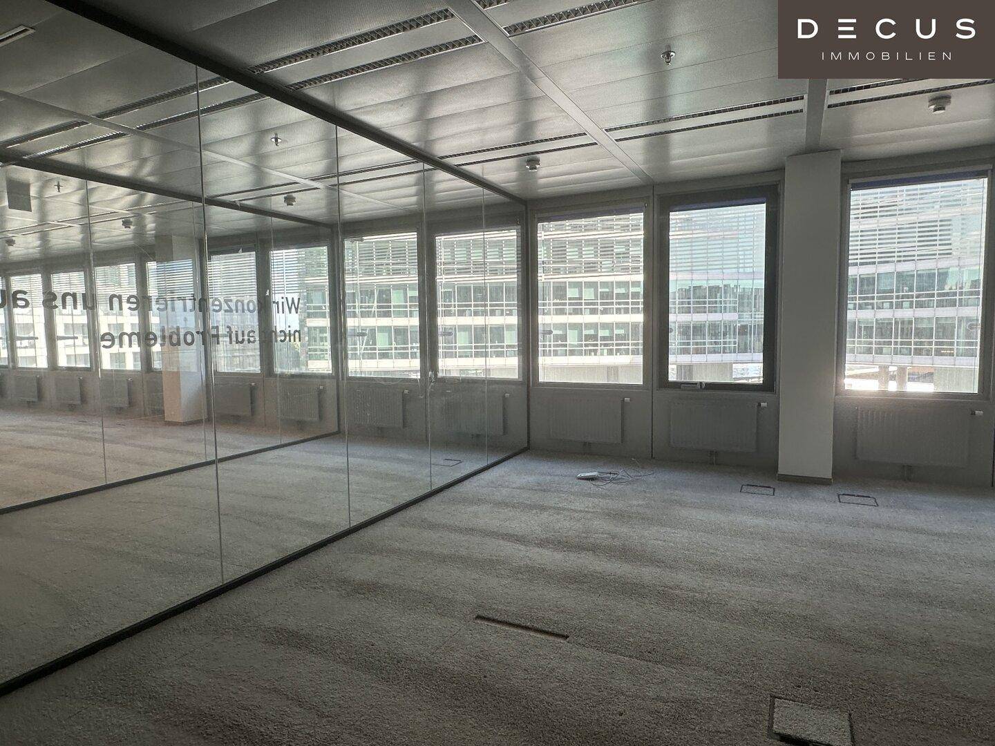 Großzügiger Bürobereich mit durchgehenden Glaswänden und Teppichboden, ideal für offene Konzepte.