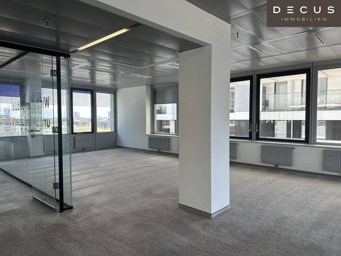 Großes, helles Büro mit Teppichboden, einer Säule und Glaswänden, die den Raum unterteilen.