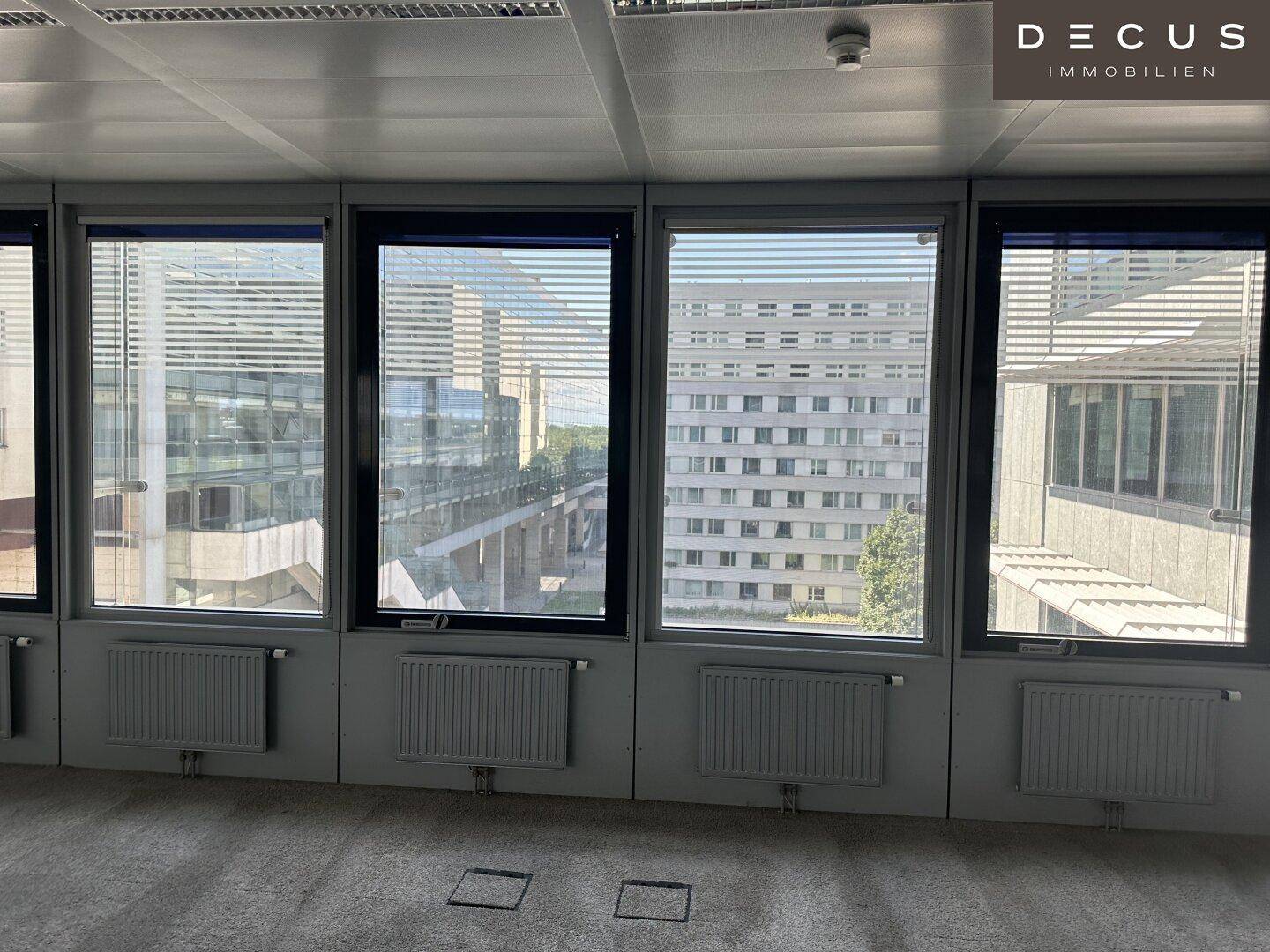 Büro mit Teppichboden und einer Reihe von Fenstern, die einen Blick auf andere Gebäude bieten.