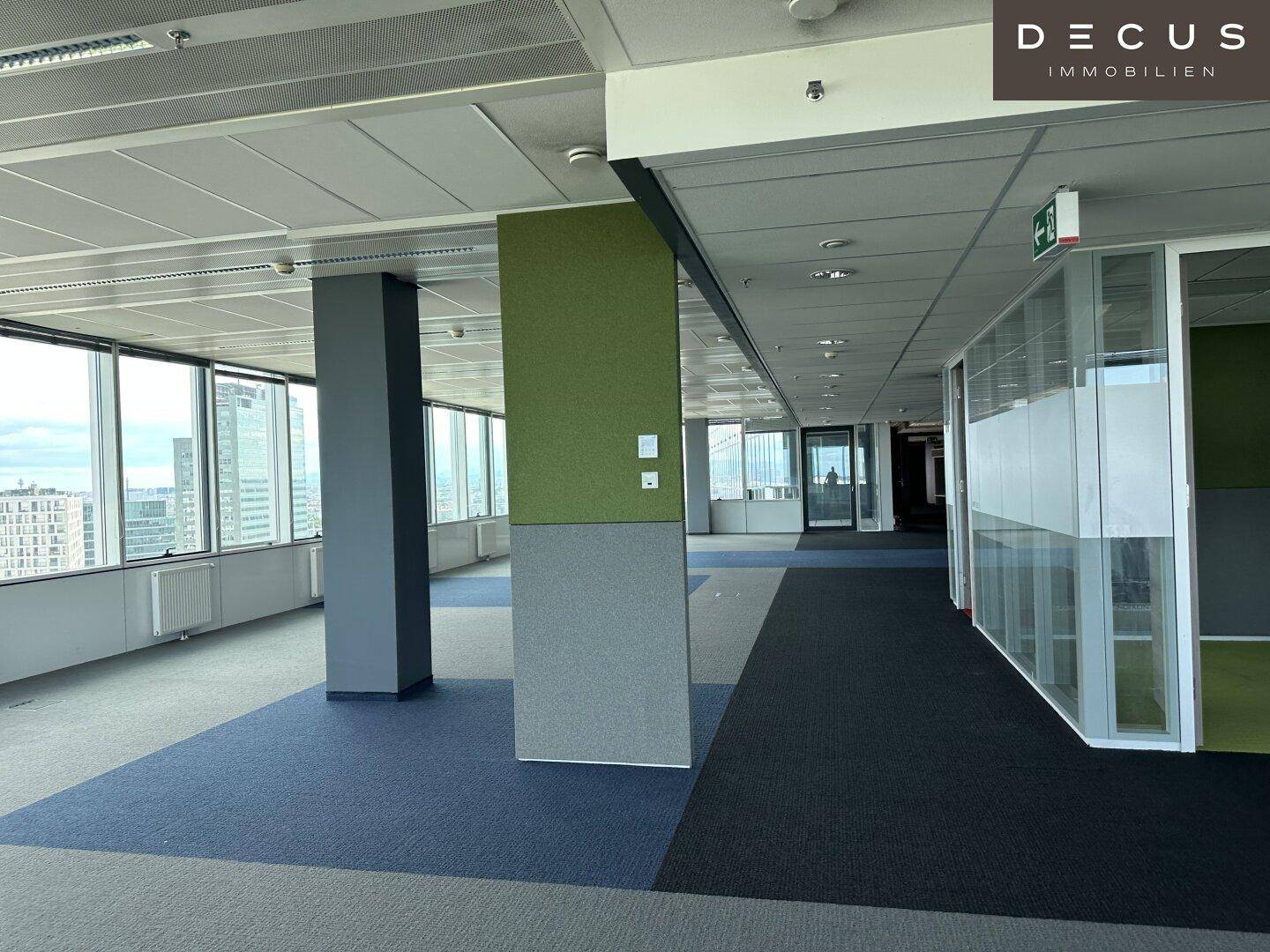 Großes, offenes Büro mit Teppichboden, Glaswänden und Blick auf die Stadt.