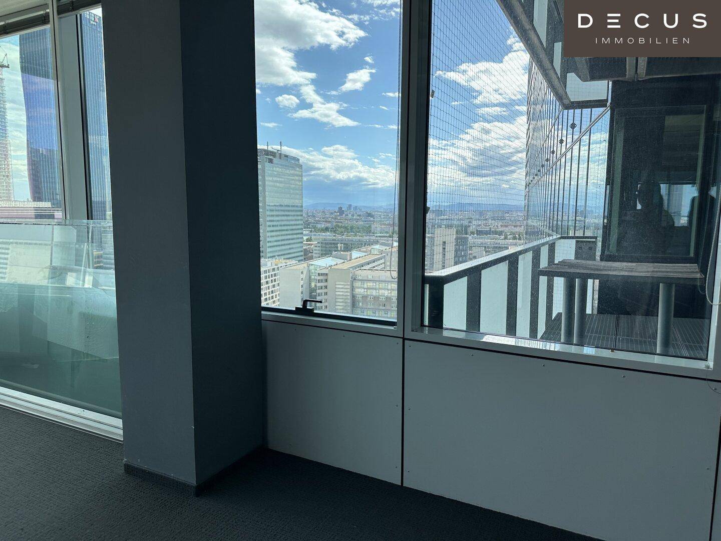Innenansicht eines Büros mit Zugang zu einem Balkon und Blick auf die Stadt.