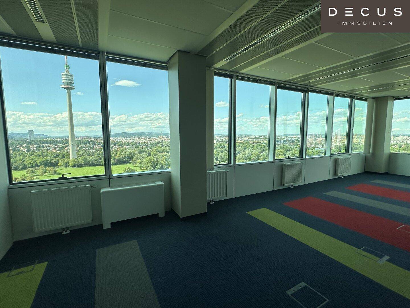 Heller Büroraum mit farbigem Teppichboden und Panoramafenstern mit Stadt- und Grünblick.