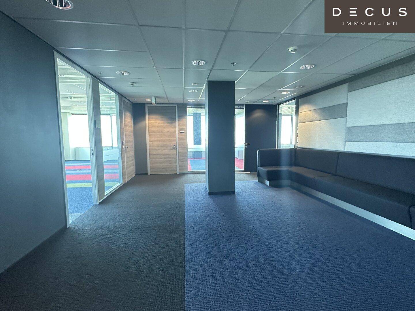 Empfangsbereich oder Wartezone in einem modernen Bürogebäude mit Sitzgelegenheiten und Teppichboden.