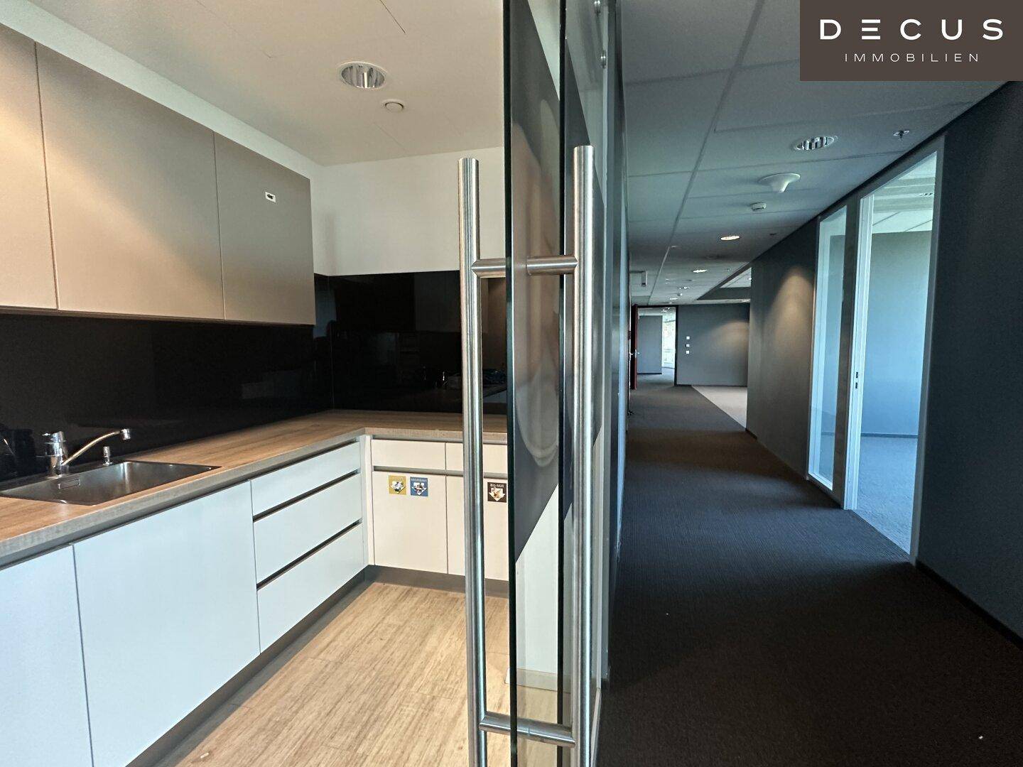 Moderne Teeküche mit Holz-Arbeitsplatte, Spüle und Schränken in einem Bürokomplex.