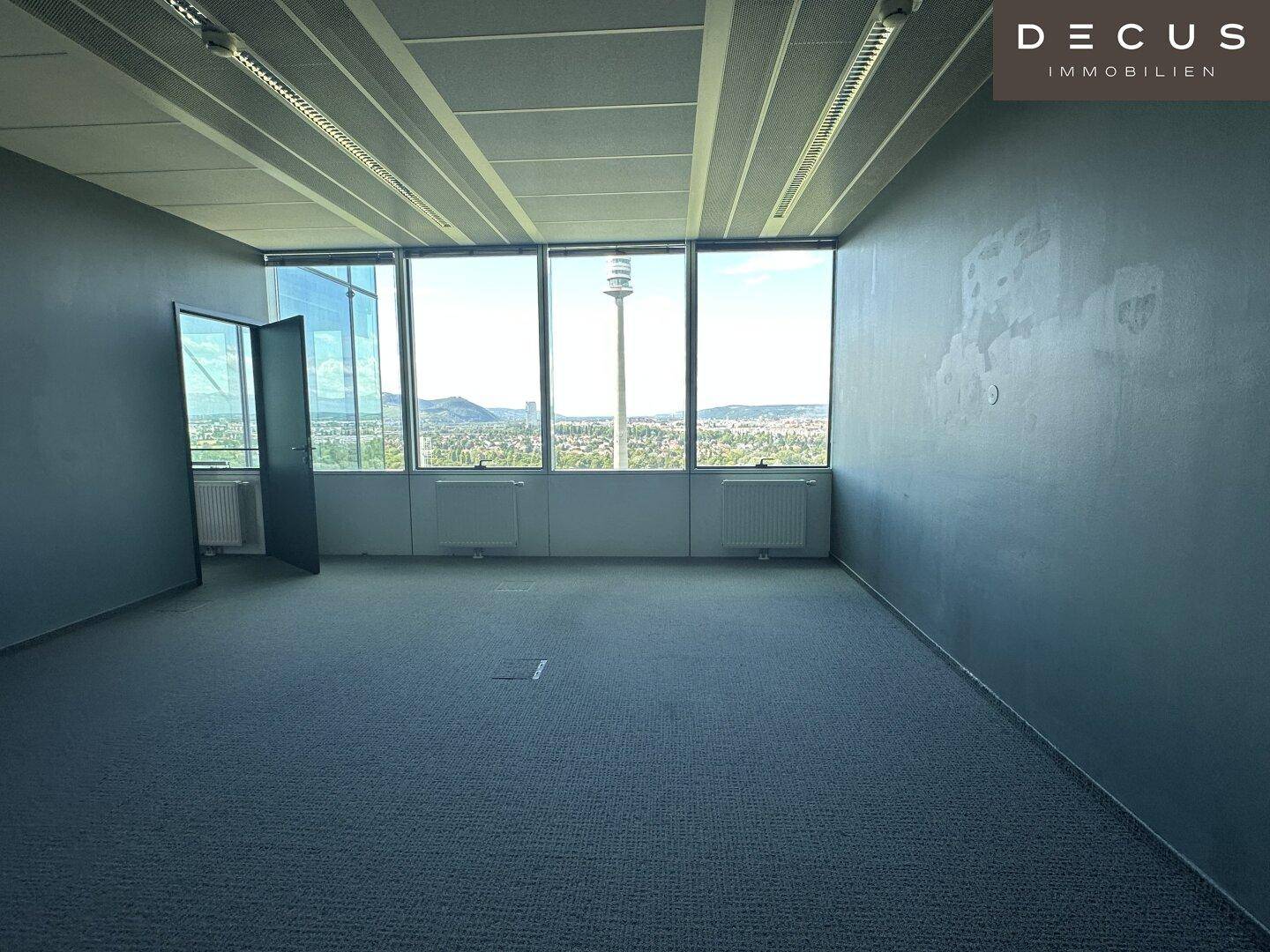 Geräumiges Büro mit Teppichboden und Panoramafenstern, die einen beeindruckenden Blick auf die Stadt ermöglichen.