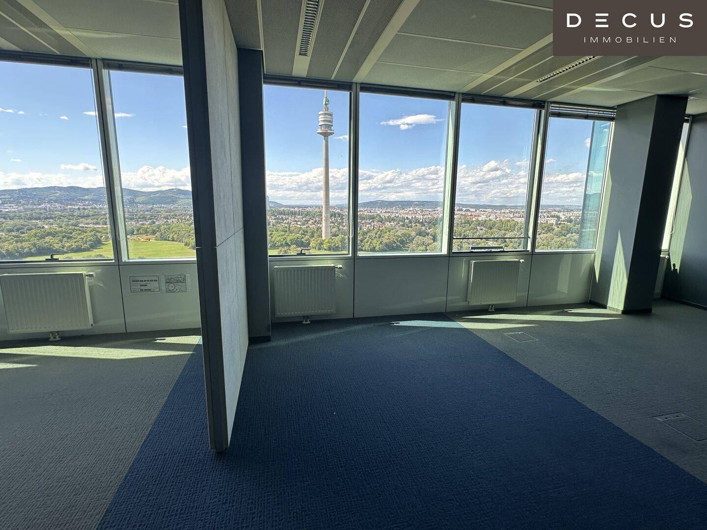 Geräumiges Büro mit großen Fenstern, die einen weiten Blick über die Stadt und den Donauturm bieten.