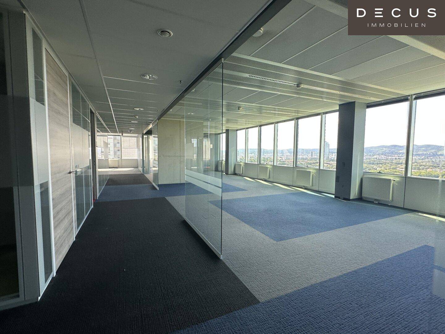 Helles Büro mit Teppichboden und raumhohen Fenstern, die eine weite Aussicht auf die Umgebung ermöglichen.