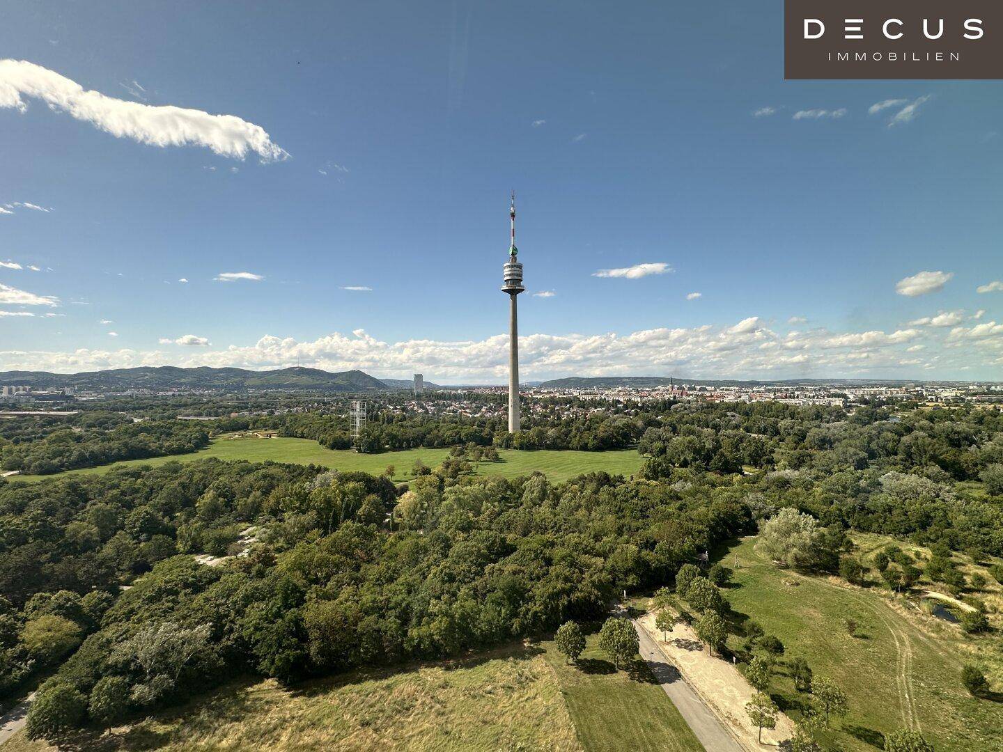 Panoramablick auf den Donauturm und die umliegende grüne Landschaft unter blauem Himmel.