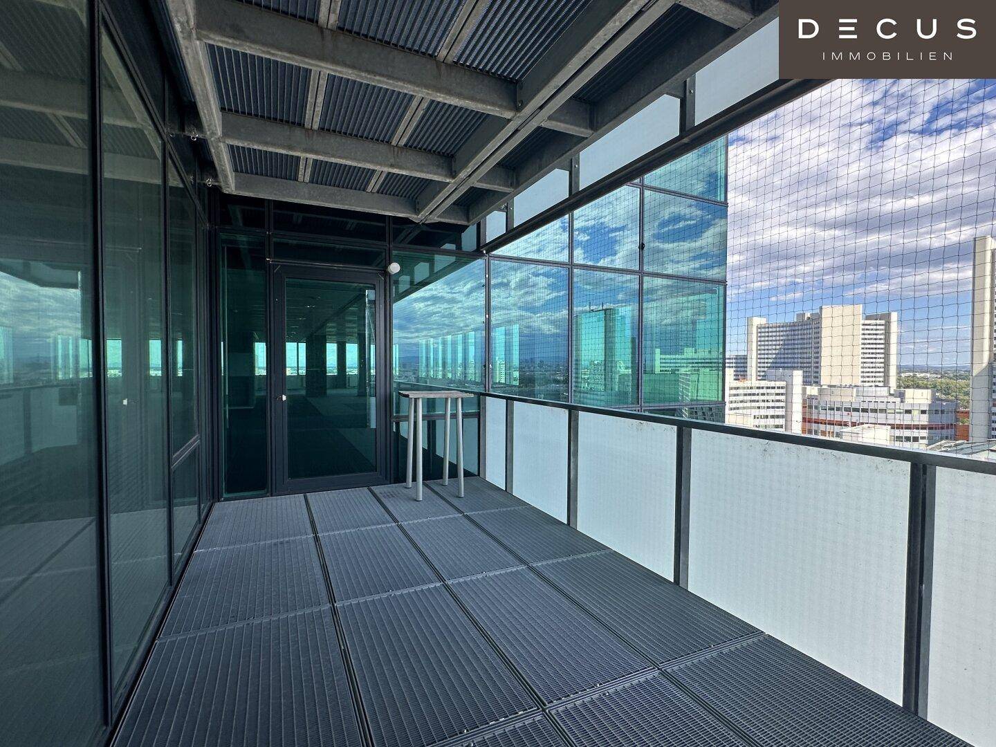 Geräumiger Balkon mit Metallboden und Glasgeländer, bietet einen weiten Blick auf die Stadt.