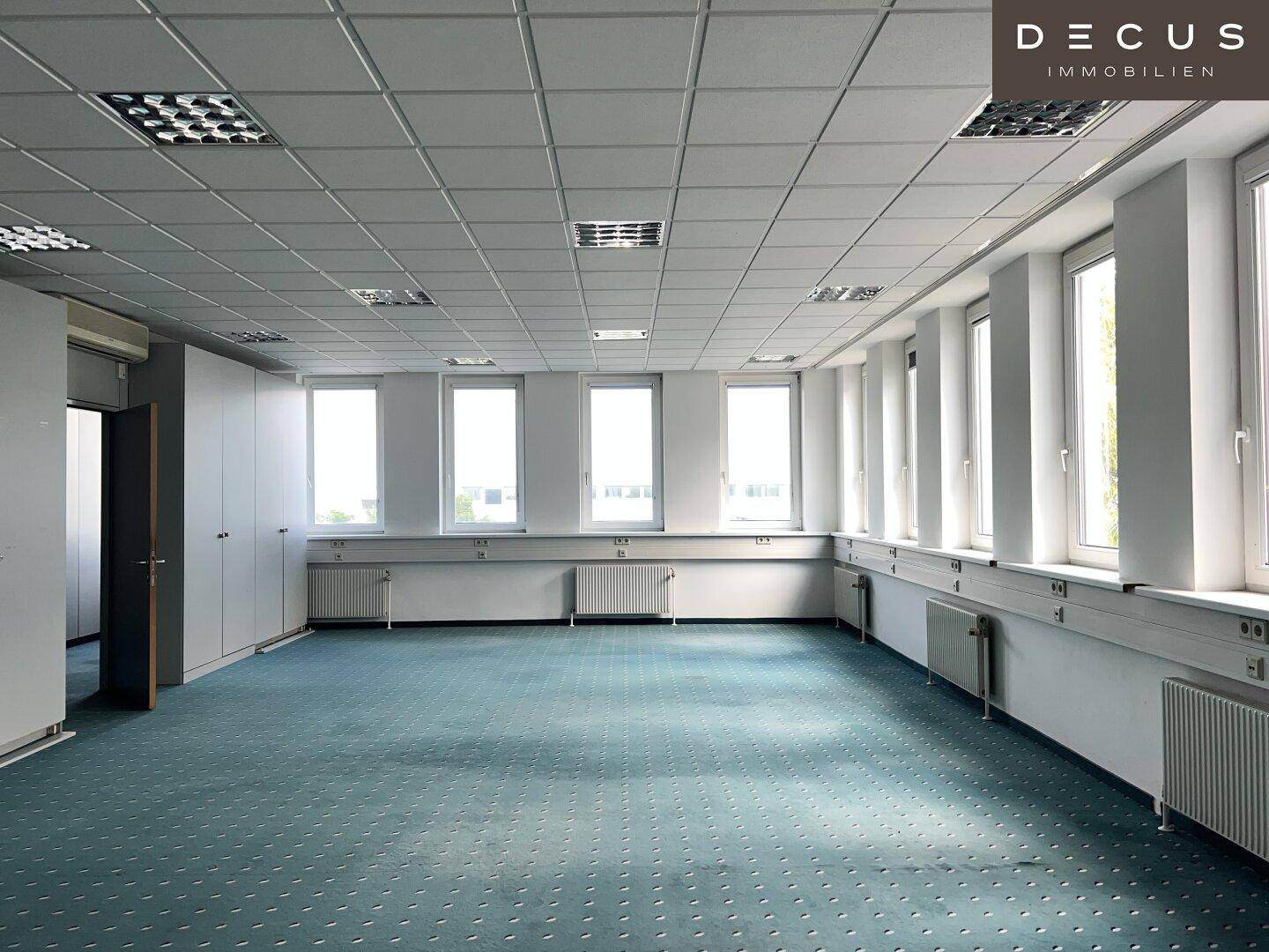 Unmöbliertes Büro mit grünem Teppich, Einbauschränken und Klimaanlage an der Wand.