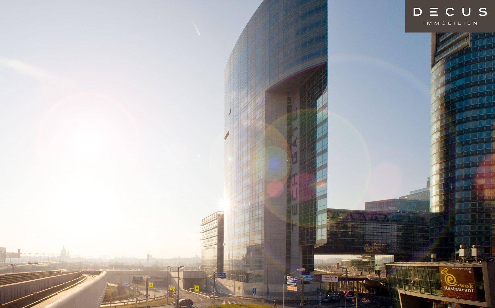 Panoramablick auf das moderne Glasgebäude bei Sonnenuntergang, umgeben von städtischer Infrastruktur und Straßen.