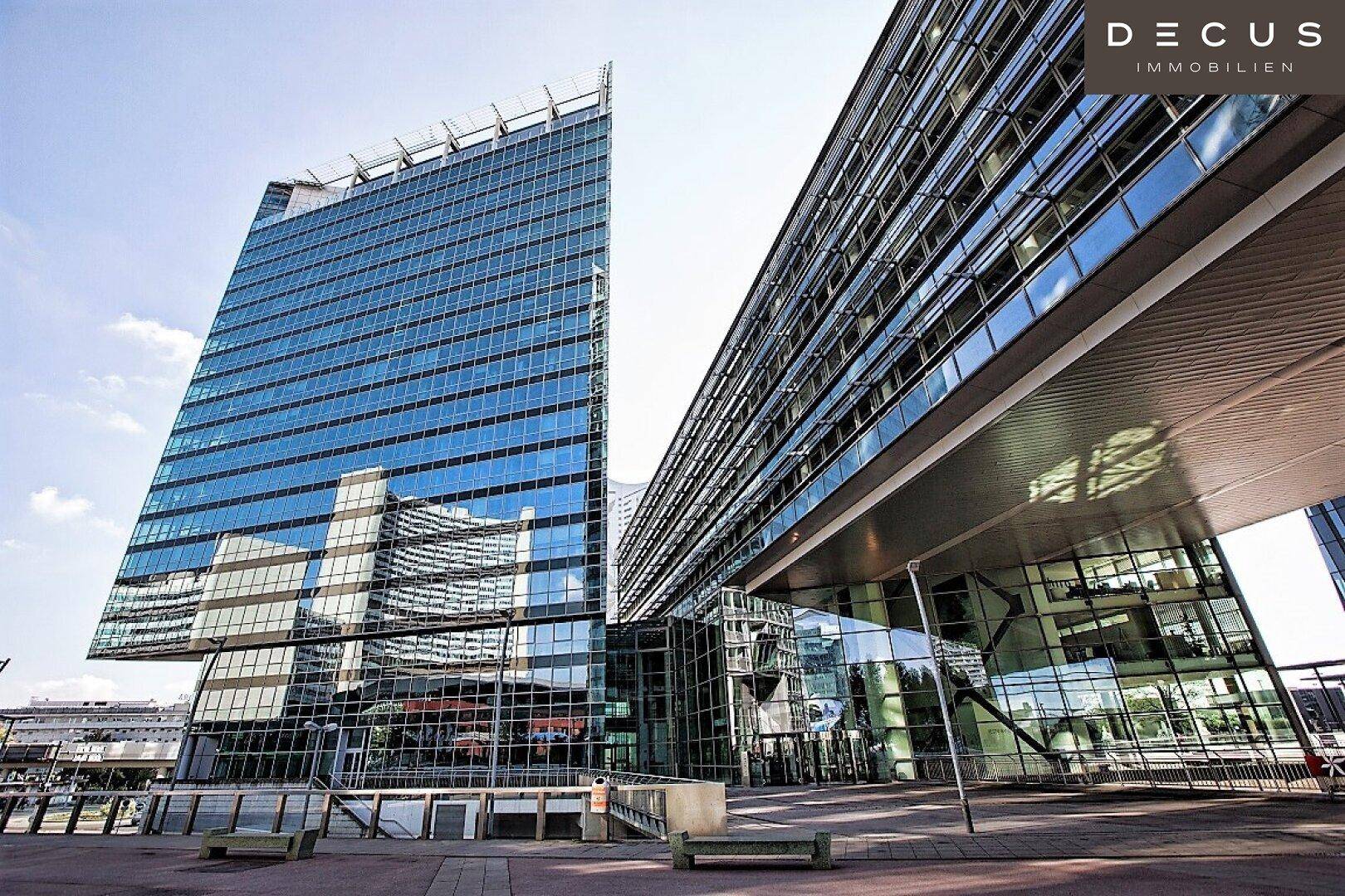 Zwei moderne Bürogebäude mit beeindruckenden Glasfassaden und architektonischen Überhängen in einer städtischen Umgebung.