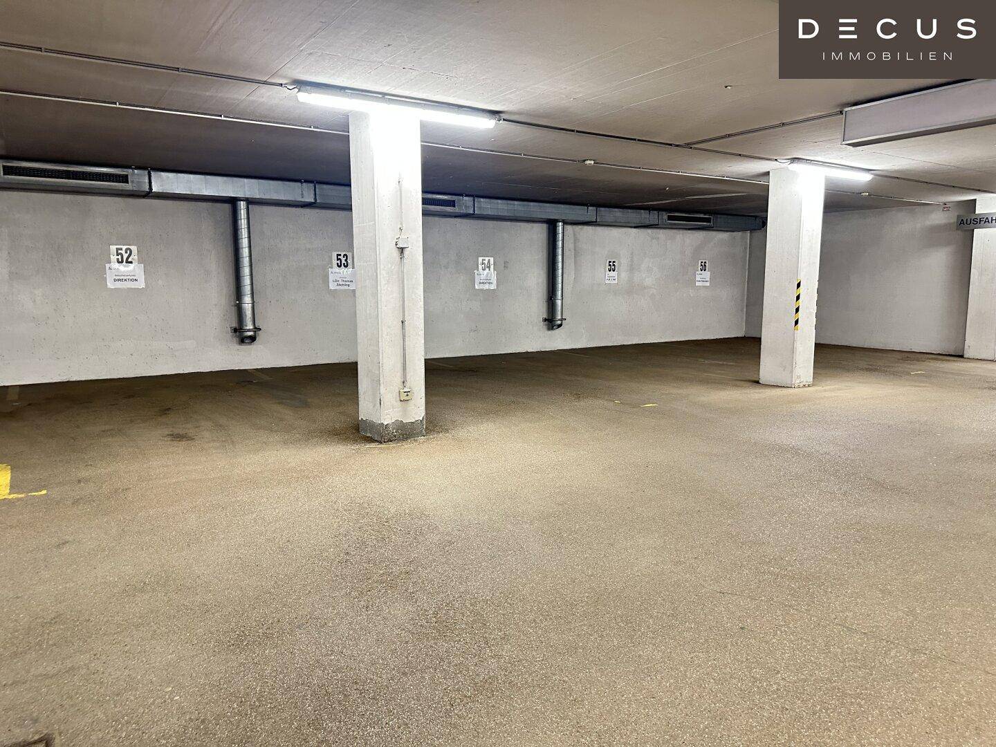 Tiefgarage mit nummerierten Stellplätzen, Betonpfeilern und Deckenbeleuchtung.