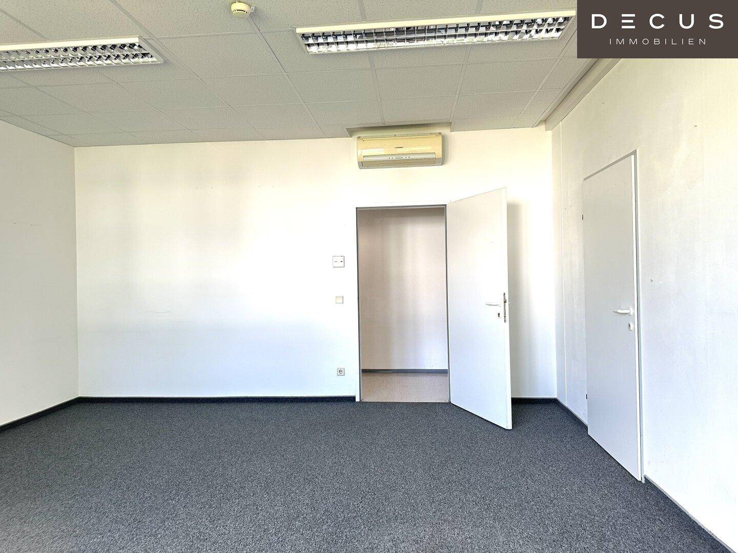 Leeres Büro mit Teppichboden, weiß gestrichenen Wänden und einer Klimaanlage an der Decke.