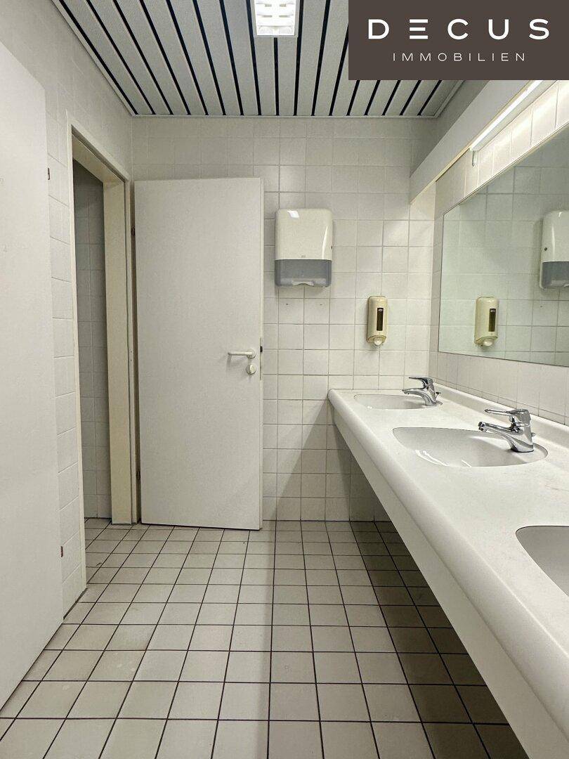 Gefliestes Badezimmer mit zwei Waschbecken, großem Spiegel und weißen Fliesen an Wänden und Boden.