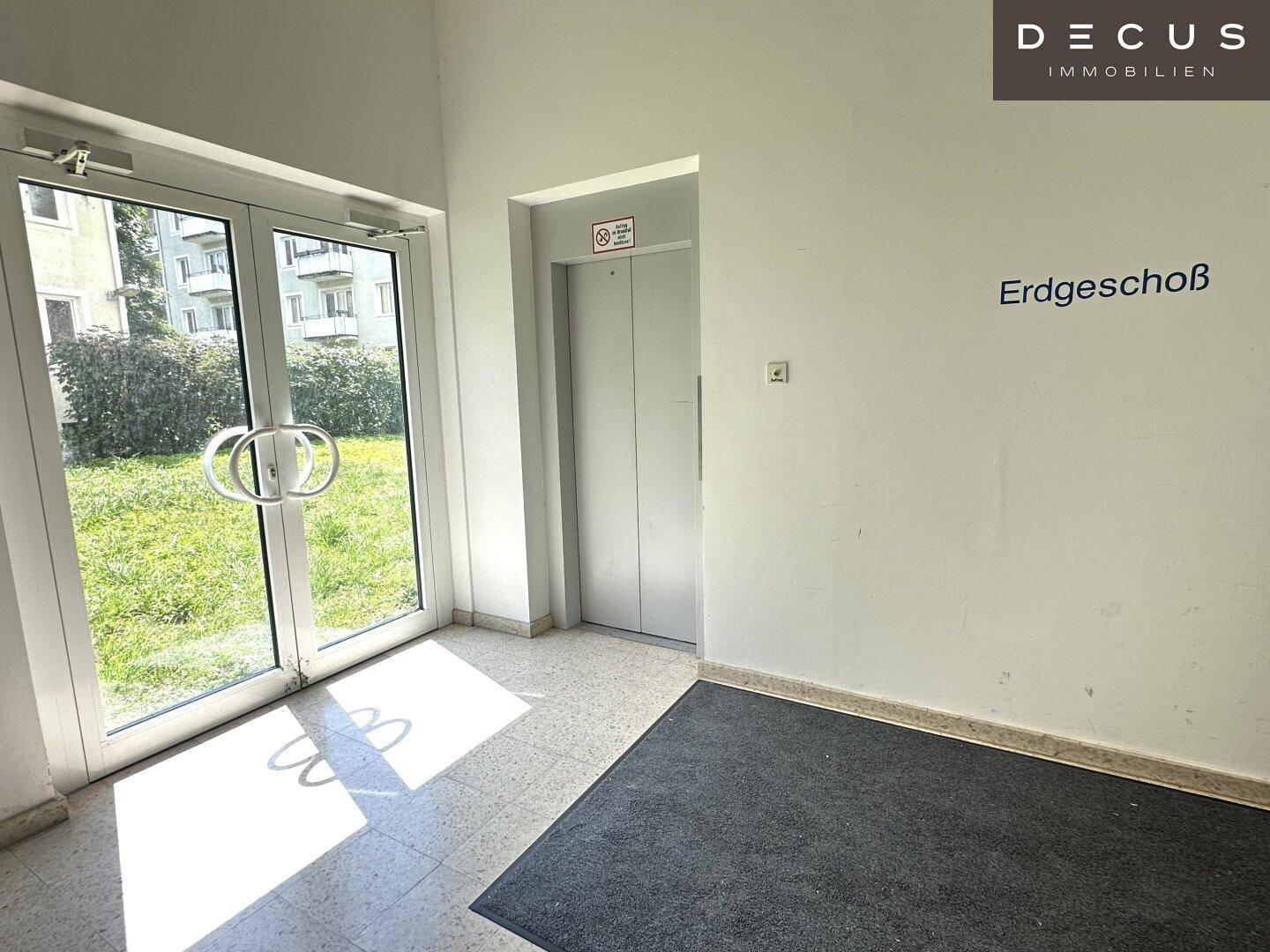 Eingangsbereich mit Glastür, Aufzug und Beschriftung 'Erdgeschoß' an der Wand.