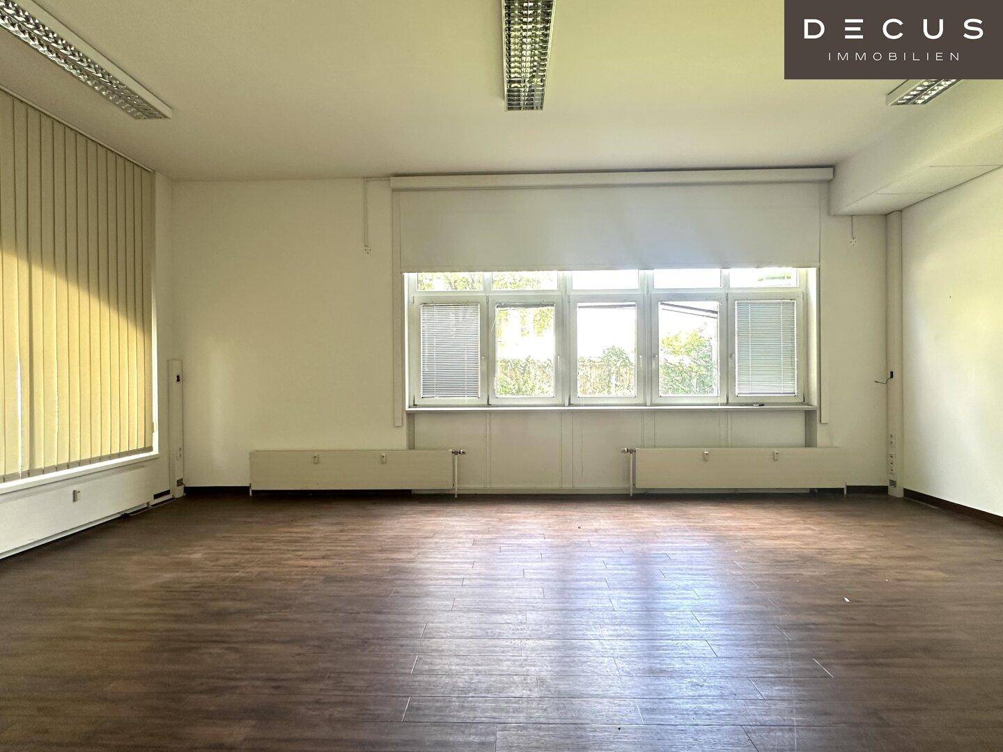 Heller Büroraum mit mehreren Fenstern und Blick ins Grüne, ideal für eine angenehme Arbeitsatmosphäre.
