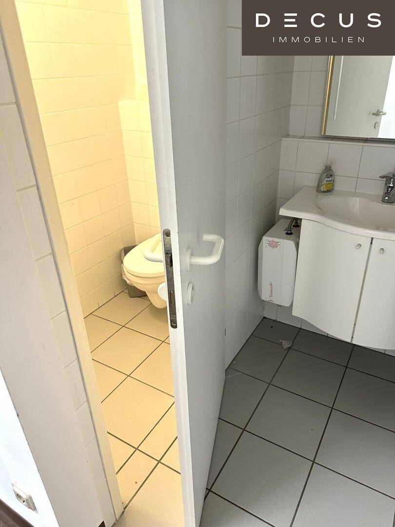Separate Toilette mit Waschbecken und Fliesenboden, sauber und funktional gestaltet.