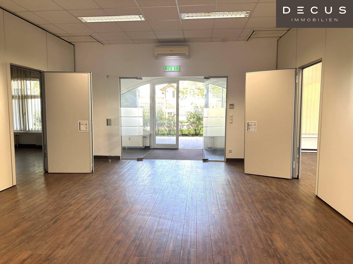 Heller Eingangsbereich eines Büros mit Glasfront und Holzboden, der viel Tageslicht hereinlässt.