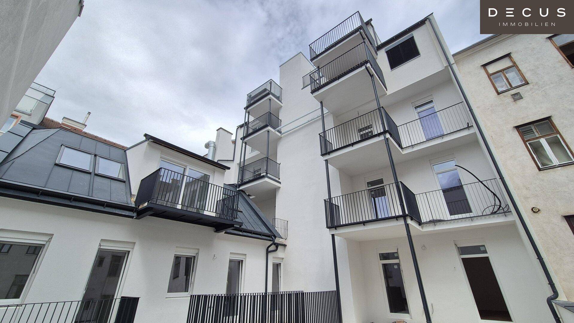 Moderne Gebäudefassade mit mehreren Balkonen und großen Fenstern unter einem bewölkten Himmel.