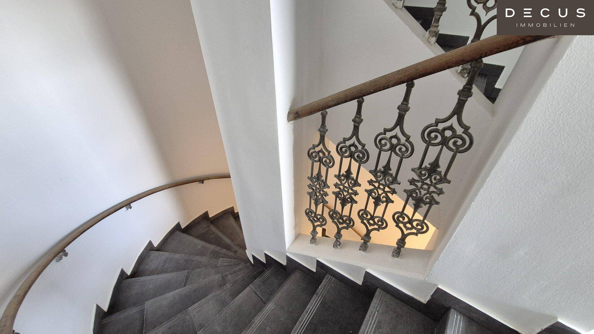 Elegante Wendeltreppe mit kunstvollem schmiedeeisernem Geländer und Steinstufen in einem Altbau.