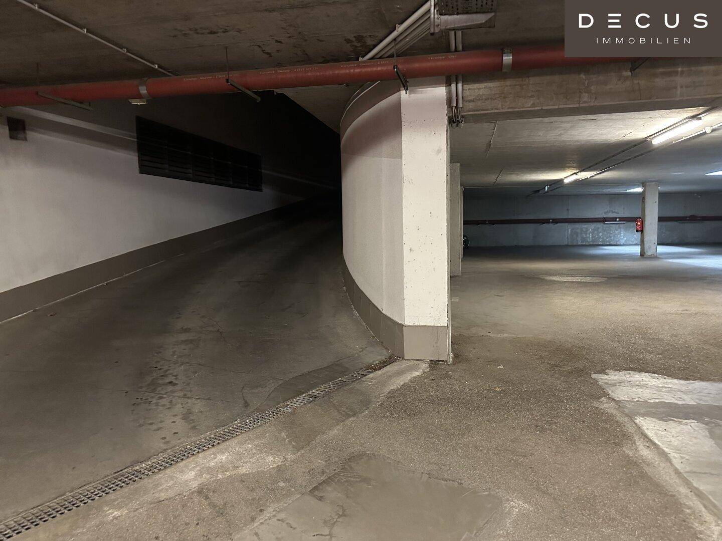 Tiefgarage mit einer geschwungenen Rampe, Betonwänden und sichtbaren Leitungen an der Decke.