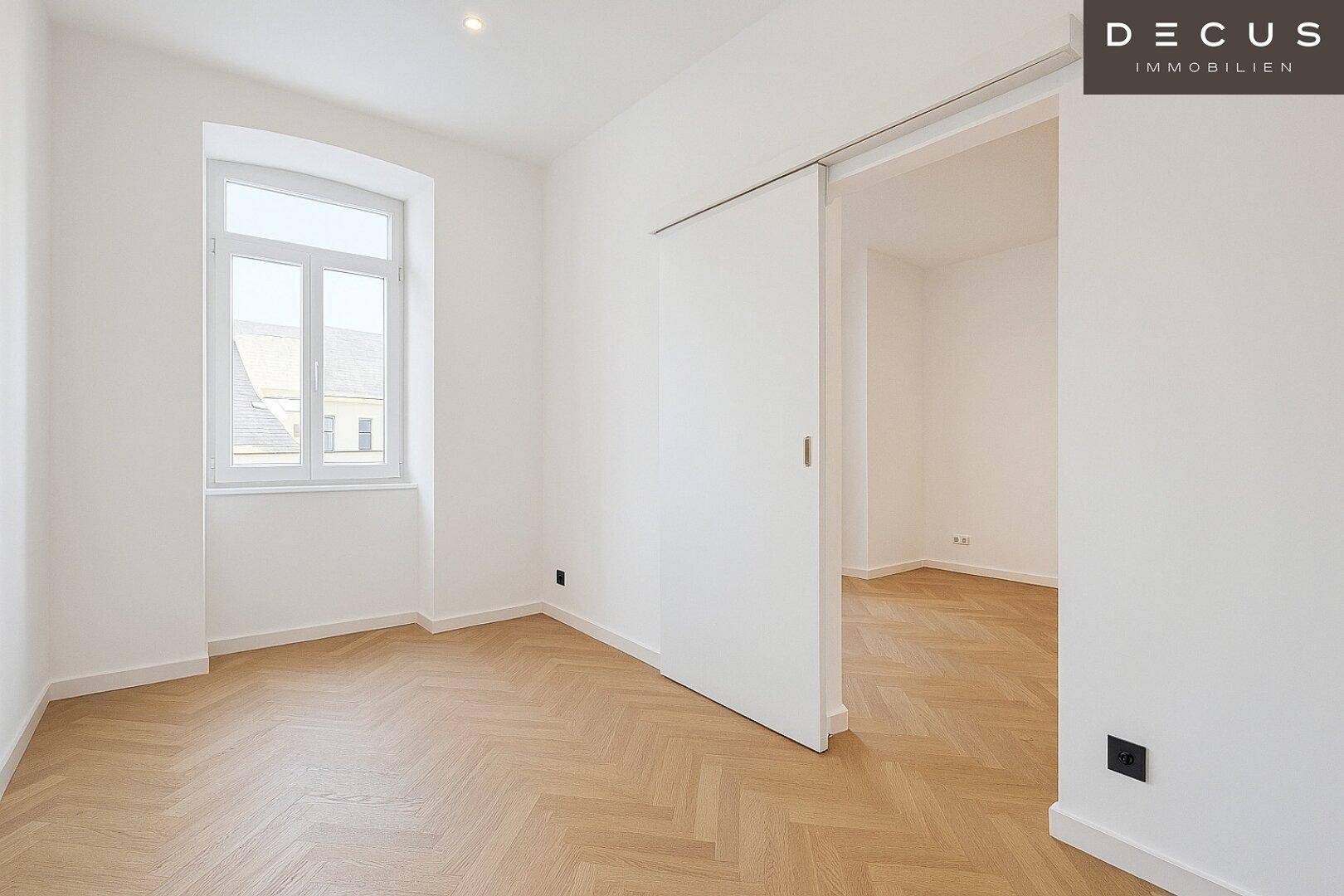 Heller Raum mit Fischgrätparkett, hohen Decken und großen Fenstern, ideal als Wohn- oder Schlafzimmer.