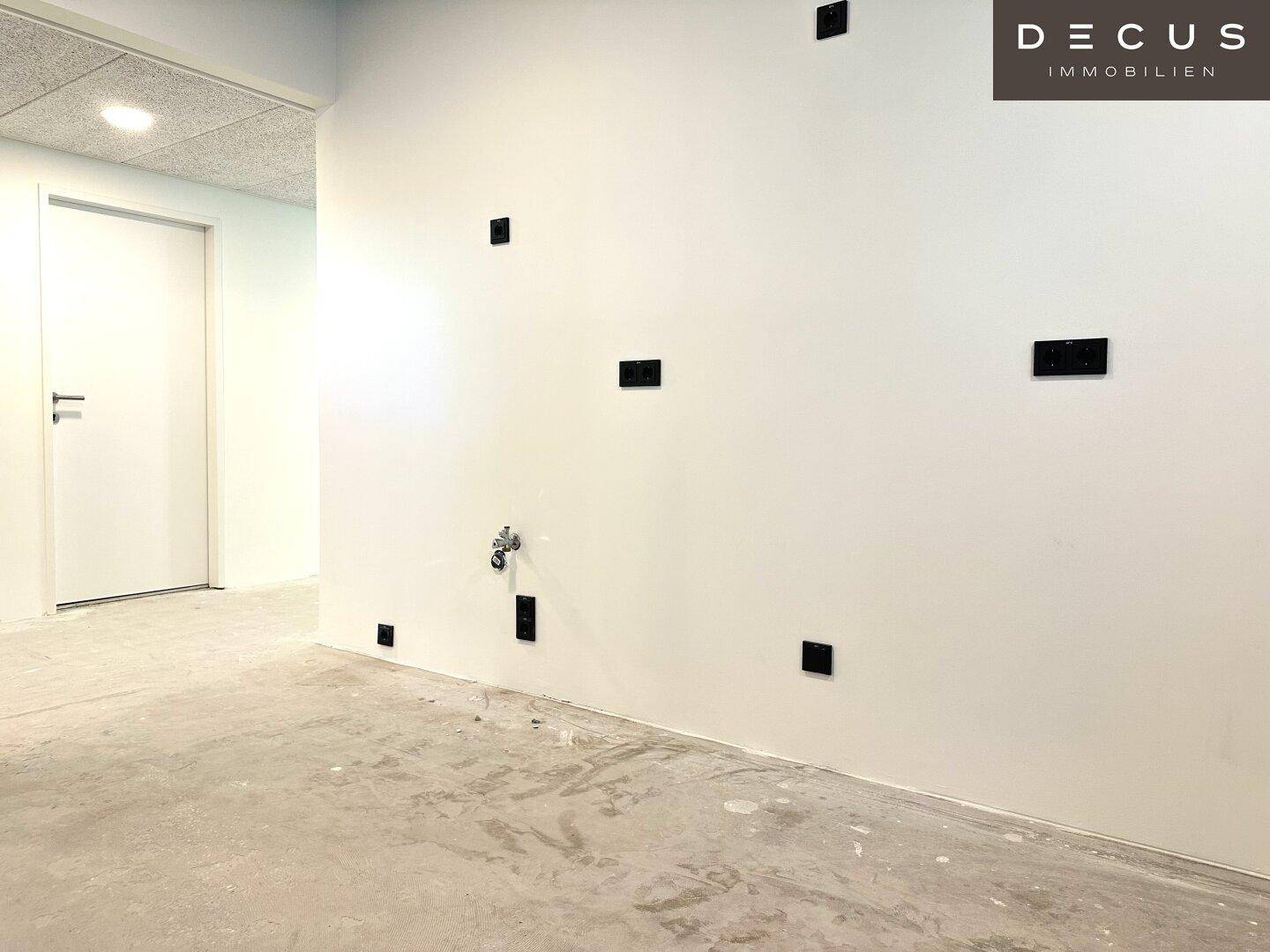 Wand in einem Büroraum mit zahlreichen Steckdosen und einem Wasseranschluss, bereit für die Installation.