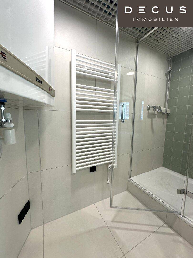 Duschbereich in einem modernen Badezimmer mit Glasabtrennung und Handtuchheizkörper.